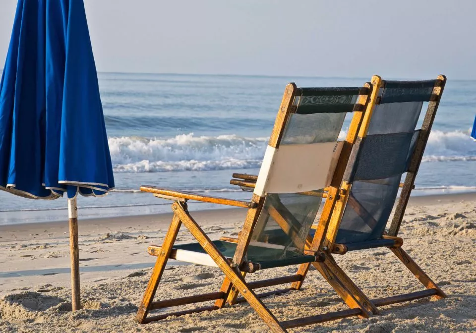 Two chairs on the beach with a blue umblrella