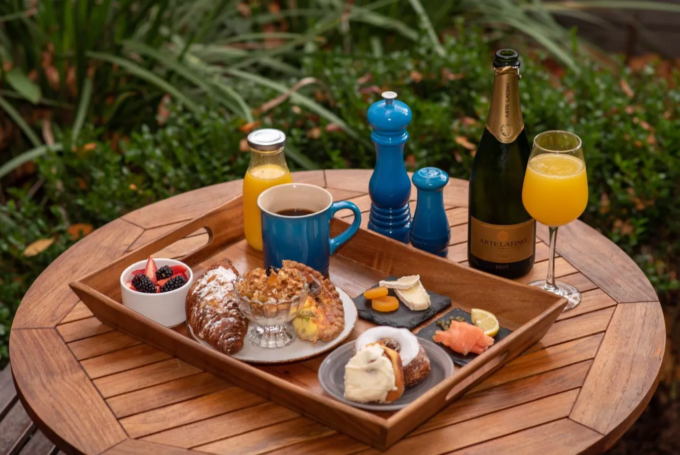 Breakfast tray on wooden table with croissants, fruit, orange juice, mimosas, and coffee